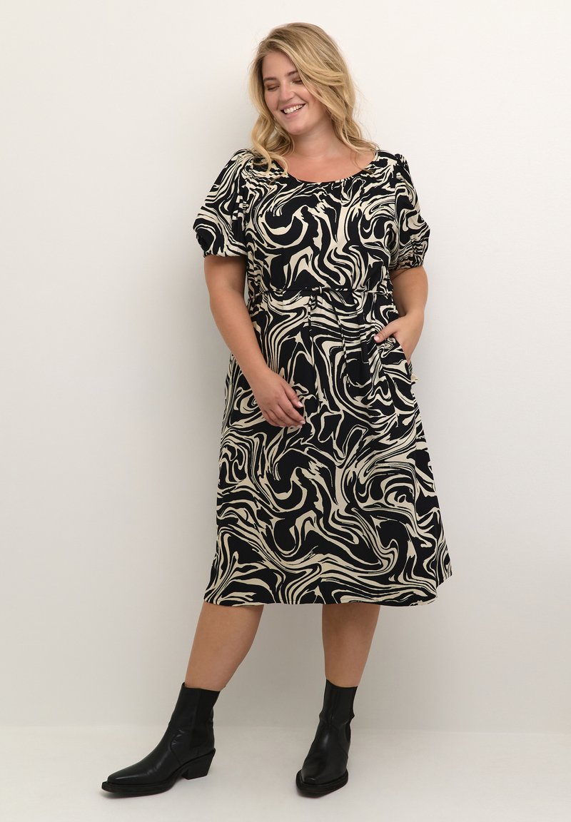 Schwarzes und cremefarbenes marmoriertes Kleid mit kurzen Puffärmeln, einem taillierten Gürtel und Taschen; kombiniert mit schwarzen Knöchelstiefeln.
