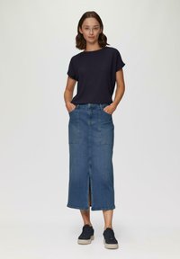 Top de manga corta azul marino combinado con una falda de mezclilla larga con bolsillos frontales y una abertura central, usada con zapatillas oscuras.