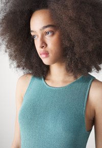 Τιρκουάζ ριγέ αμάνικο μπλουζάκι με στρογγυλή λαιμόκοψη, που τονίζει μια λεία υφή με υποσελήνιο λαμπερό φινίρισμα.