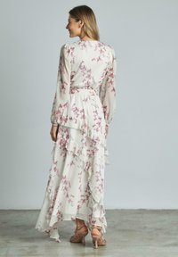 Lungo vestito floreale con sfondo bianco e motivi floreali rosa, strati arricciati e maniche lunghe. Abbinato a sandali con tacco.