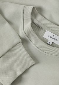  Lichtgroene sweatshirt met ribgebreide kraag en boorden. Zachte textuur, label zichtbaar met "TNTUUM" en maat "S." Eenvoudig, minimalistisch ontwerp.