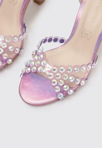Sandalias transparentes moradas con un acabado brillante, que presentan filas de piedras brillantes circulares y un diseño de punta abierta redondeada.