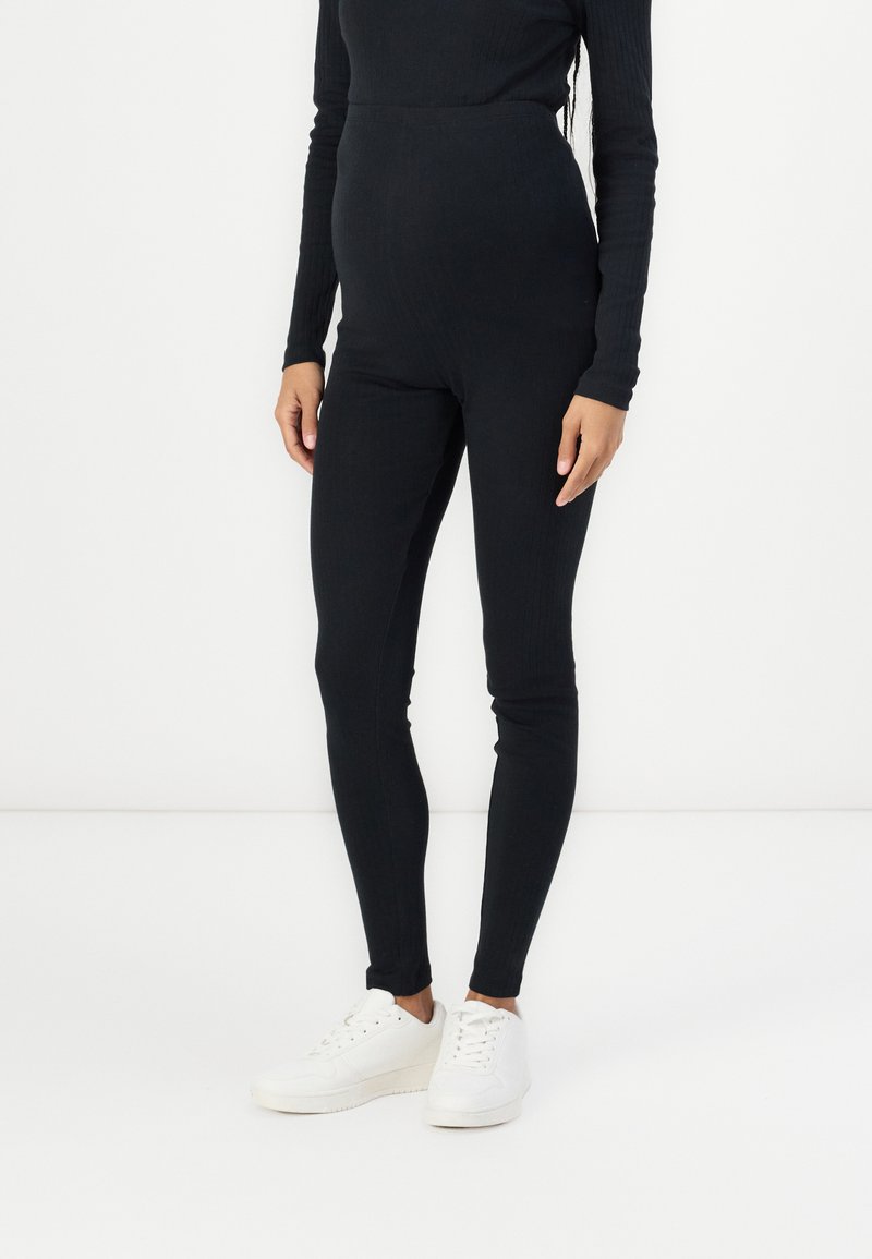Leggings de maternité noirs à côtes avec taille haute. Fabriqués à partir d'un tissu extensible, présentant une texture douce et une silhouette ajustée.