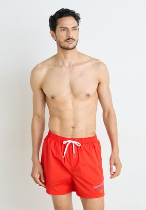 Rote Badeshorts aus leichtem Stoff, mit einem elastischen Bund und weißen Kordelzügen. Auf der Seite ist ein besticktes Logo vorhanden.