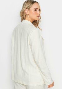 Blazer bianco in lino con vestibilità morbida, rever a punta e maniche lunghe. La parte posteriore presenta dettagli semplici e una texture liscia.