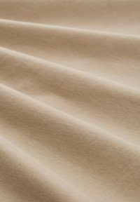 Bežani pamučni materijal s glatkom teksturom, s blagim naborima i suptilnim sjajem, koji prikazuje svoju laganu i meku pojavu.