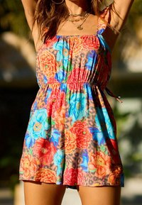 Kombinezon w kwiatowy wzór z mieszanką czerwonych, niebieskich i pomarańczowych kwiatów na brązowym tle w panterkę, z ramiączkami typu spaghetti i elastycznym pasem.