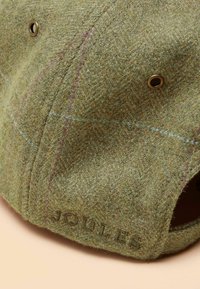 Șapcă verde de tweed cu model în zigzag, ochiuri aurii și marcaj în relief "JOULES". Textură moale cu fire multicolore.