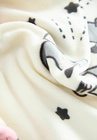 Fleece-Decke in Creme mit weichem Textur, versehen mit schwarzen Sternen und illustrierten Mustern. Leicht zerknittert, was den Fluss des Stoffes zur Geltung bringt.