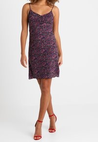 Květinové šaty s fialovým základem a malými růžovými květy, s přiléhavým tělem, tenkými ramínky a zvlněným lemem. Nosit s červenými podpatky.