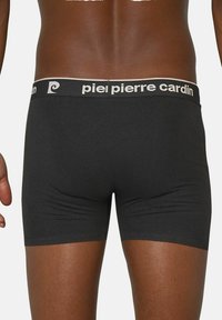 Black boxer briefs with a contrasting beige waistband featuring the brand name "piel pierre cardin" in repeating text. Smooth fabric texture.