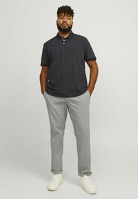 Navy polo shirt with white polka dots and a collar, paired with light gray trousers and white sneakers. Smooth fabric, casual design.