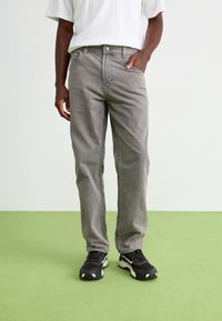 Grå denimbukser med rett ben-design, som har frontlommer og glidelås, kombinert med svarte joggesko.