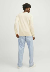 Camisa de manga larga beige claro con un ajuste relajado, combinada con vaqueros de pierna ancha azul claro y zapatillas blancas, vista desde la parte posterior.