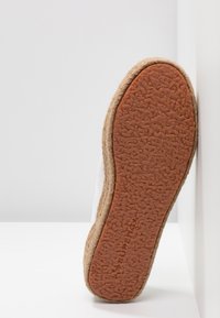 White shoe with a textured rubber sole and jute midsole. The outsole is brown with a raised pattern for grip.