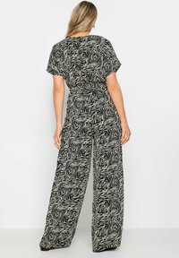 Mono de rayas negro y crema con un corte holgado, mangas cortas, cintura elástica y pantalones de pierna ancha que presentan un prominente patrón de estampado animal.