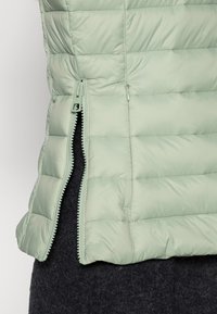 Gilet imbottito verde chiaro con texture trapuntata, zip laterale e un design leggermente accorciato, caratterizzato da una finitura morbida e opaca.