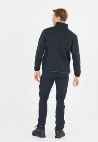 Giacca zip-up grigio scuro con colletto alto, abbinata a pantaloni neri e stivali neri. Tessuto morbido, design aderente, accessori hardware minimi.