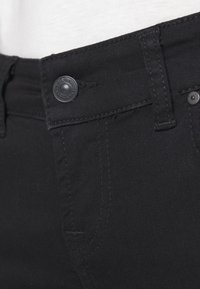 Jeans de mezclilla negra con cierre de botón y cremallera. Las características incluyen una textura suave y sutiles acentos de costura. Vista en primer plano de la cintura.