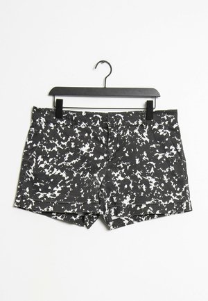 Schwarz-weiß gemusterte abstrakte Damenshorts mit Gürtelschlaufen, Vordertaschen und Reißverschluss, die an einem schwarzen Kleiderbügel hängen.