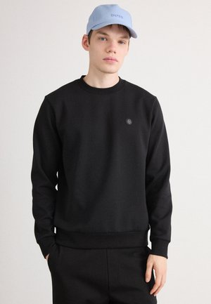 Svart hettegenser med rund hals og ribbede mansjetter, med en liten logo på brystet. Kombinert med en lys blå caps.