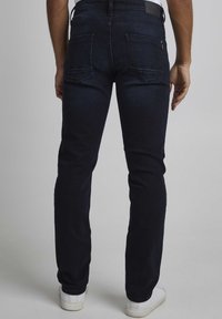 Jeans de mezclilla azul oscuro con un corte recto, que muestran dos bolsillos traseros y una textura suave. Se llevan zapatillas blancas.