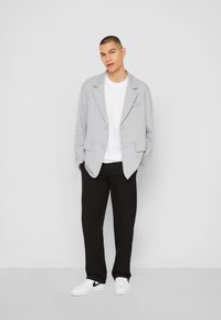 Grå stickad blazer med sjalkrage, två framfickor, bärs över en vit t-shirt och svarta byxor, tillsammans med vita sneakers.