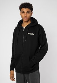 Black zip-up hoodie made of soft fabric, featuring a front pocket, drawstring hood, and white printed text “HIGH STANDARDS ALLOWED LOW IMPACT.”