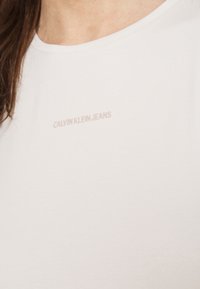 Bílé bavlněné tričko s kulatým výstřihem, krátkými rukávy a jemným světle růžovým vyšitým logem "CALVIN KLEIN JEANS" na přední straně.