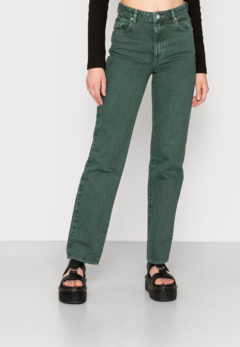 Jeans verdes de cintura alta feitos de denim, com uma leve textura, corte de perna reta e design de cinco bolsos, combinados com sandálias de plataforma pretas.