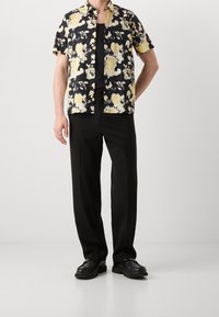 Camisa de manga corta con botones, fondo negro y estampado floral amarillo, combinada con pantalones negros y zapatos negros.