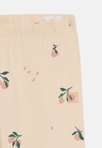 Lichtbeige stof met een zachte textuur, voorzien van een oranje patroon en groene bladeren, evenals een klein logo-label op de tailleband.