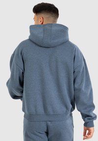 Felpa grigia con cappuccio, dal fitting rilassato, texture morbida, polsini e vita a coste; presenta un cappuccio con dettagli di cucitura.