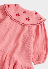 Różowa sukienka z fakturą, z bufkami na rękawach, marszczonym dołem i haftowanym wzorem wiśni na szerokim, falistym kołnierzu z czerwoną lamówką.