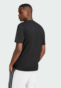 Camiseta negra de algodón con mangas cortas y corte regular. Diseño liso con escote redondo, sin logotipos ni patrones visibles. Pantalones blancos con rayas.