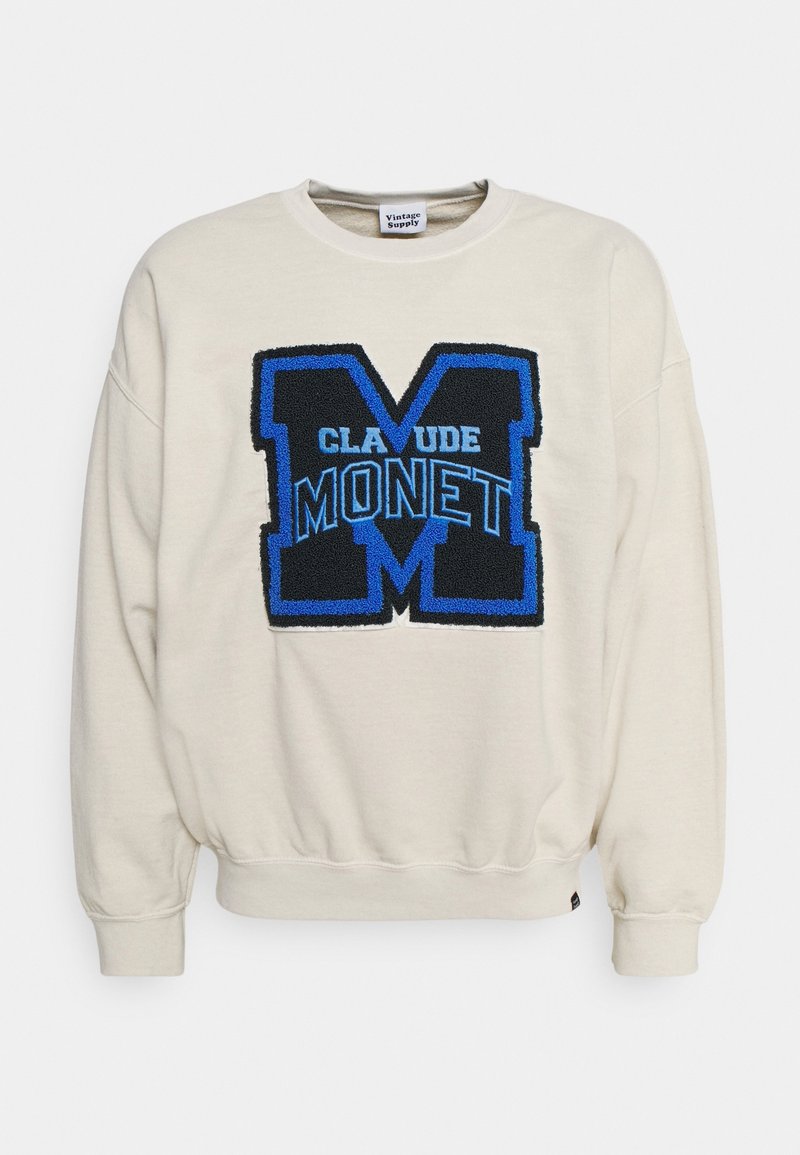Cremefärgad sweatshirt med en strukturerad blå och svart "M"-design samt texten "CLAUDE MONET". Har rund hals och ribbade muddärmar.