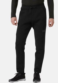 Pantalones de chándal negros hechos de una tela suave, con cintura ajustable, piernas estrechas y un logo sutil en el lateral.