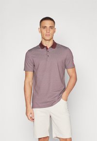 Polo triko s vínovým a bílým vzorem, s vínovým límečkem. Krátké rukávy a slim fit, v kombinaci s bledě béžovými šortkami.