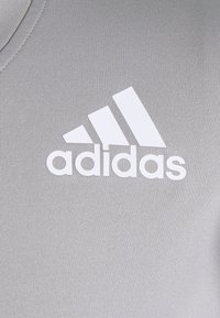 Harmaa urheilupaita, jossa on uritettu pinta ja valkoinen Adidas-logo kolmella vinoviivalla.