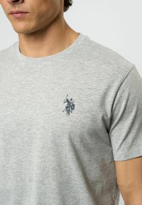 Grå bomullströja med en liten mörkblå polo-spelargrafik på vänster bröst. Klassisk rund hals och korta ärmar.