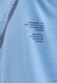 Ανοιχτό μπλε ύφασμα με σκούρο μπλε κείμενο που αναφέρει ότι το ένδυμα έχει σχεδιαστεί για αθλητές πρωταθλήματος και σχεδιάστηκε στα κεντρικά γραφεία της Nike στο Μπίβερτον, Όρεγκον.