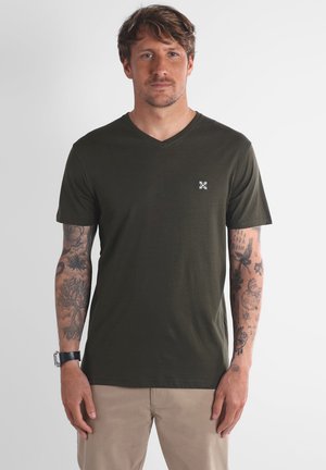 T-shirt vert olive en V fabriqué en tissu doux, avec un petit logo blanc sur la poitrine gauche et des manches courtes.