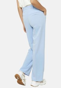 Svetlo modri hlače iz gladkega materiala, s pravimi nogavicami, stranskimi žepi in pasom, v kombinaciji z belimi teniskami.