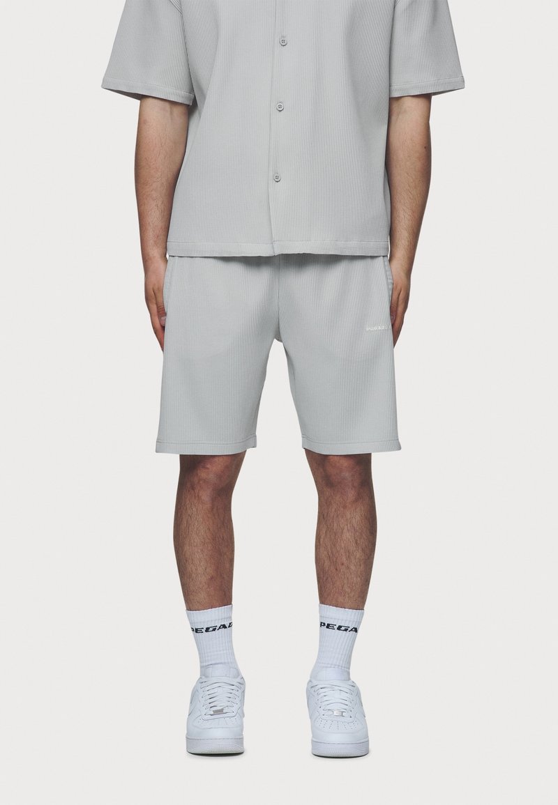 Chemise grise à manches courtes côtelée avec boutons, associée à un short assorti. Des baskets blanches et des chaussettes montantes complètent le look.