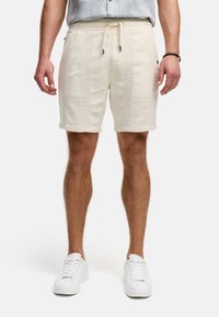 Helle beige Shorts aus strukturiertem Stoff mit einem Kordelzugbund. Verfügt über Seitentaschen und umschlagbare Säume. Getragen mit weißen Sneakers.
