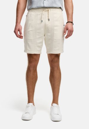 Helle beige Shorts aus strukturiertem Stoff mit einem Kordelzugbund. Verfügt über Seitentaschen und umschlagbare Säume. Getragen mit weißen Sneakers.