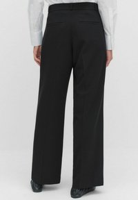 Zwarte wijde broek met een gladde stof, voorzien van twee achterzakken en een platte tailleband. De zoom ligt boven de schoenhoogte.