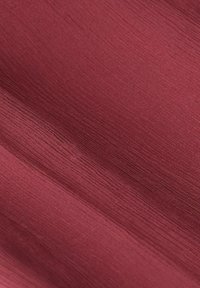 Un tissu texturé d'un profond bordeaux, avec un subtil éclat et des lignes diagonales, présente une surface lisse avec un léger éclat.