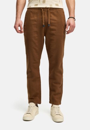 Pantalones jogger marrones y texturizados con cintura elástica y cordón. Presentan bolsillos laterales y un diseño de pierna tapered. Combinados con zapatillas ligeras.
