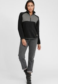 Mustam fleece-pullover, millepikendiga halli kanga ülemine osa, pool tõmblukk kaeluses ja väike logodetail allääres. Kombineeritud hallide teksade ja mustade saapatega.